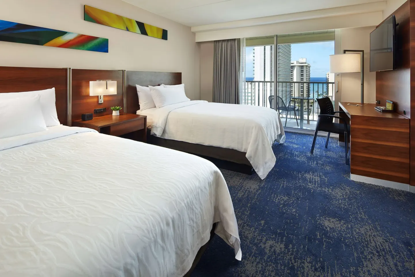 Accessible suite room with two beds, desk, balcony, and ocean glimpse at Hilton Garden Inn Waikiki Beach.
