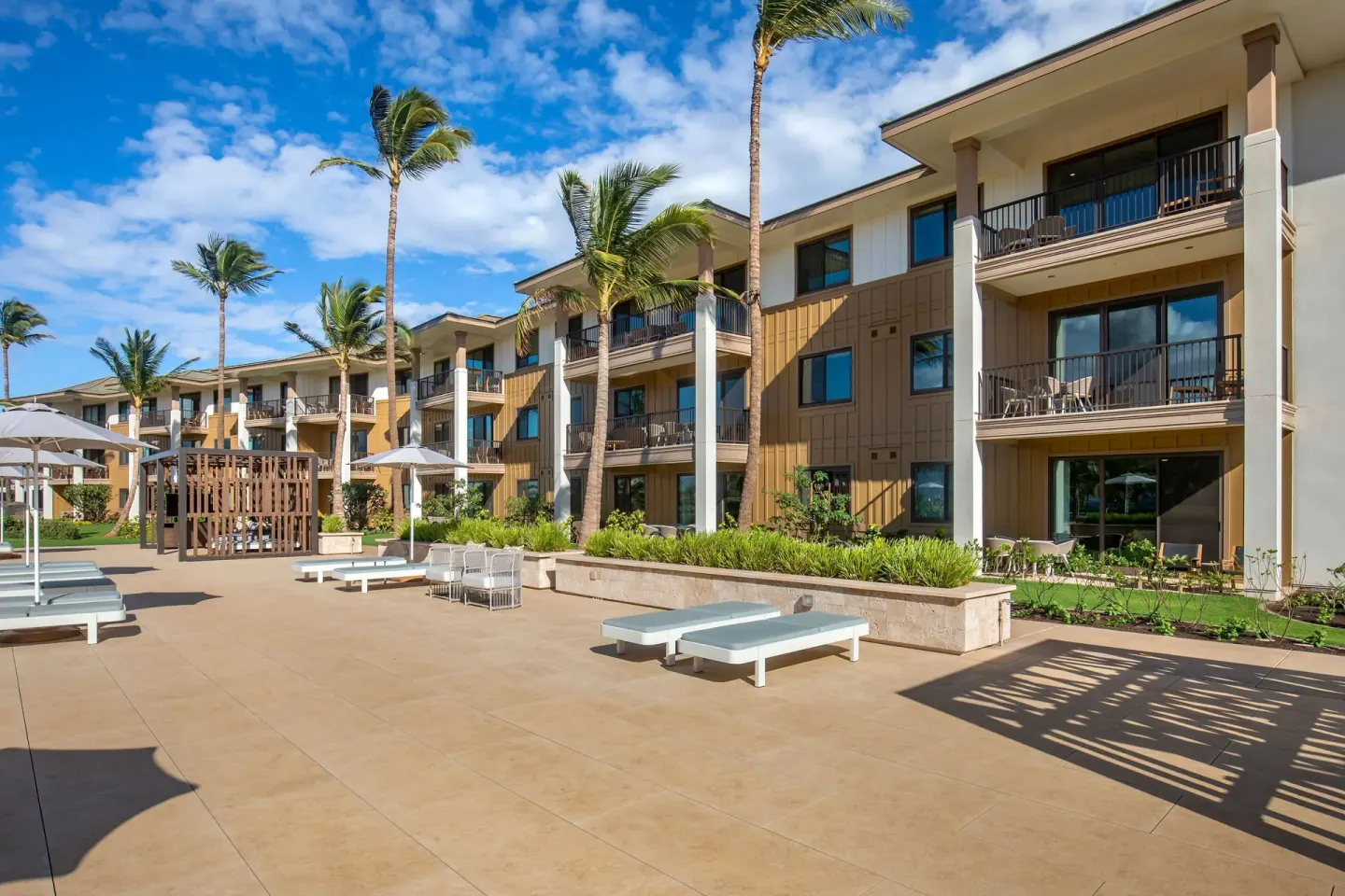 Resort courtyard at Hilton Grand Vacations Club Maui Bay Villas with balconies, loungers, and palm trees.