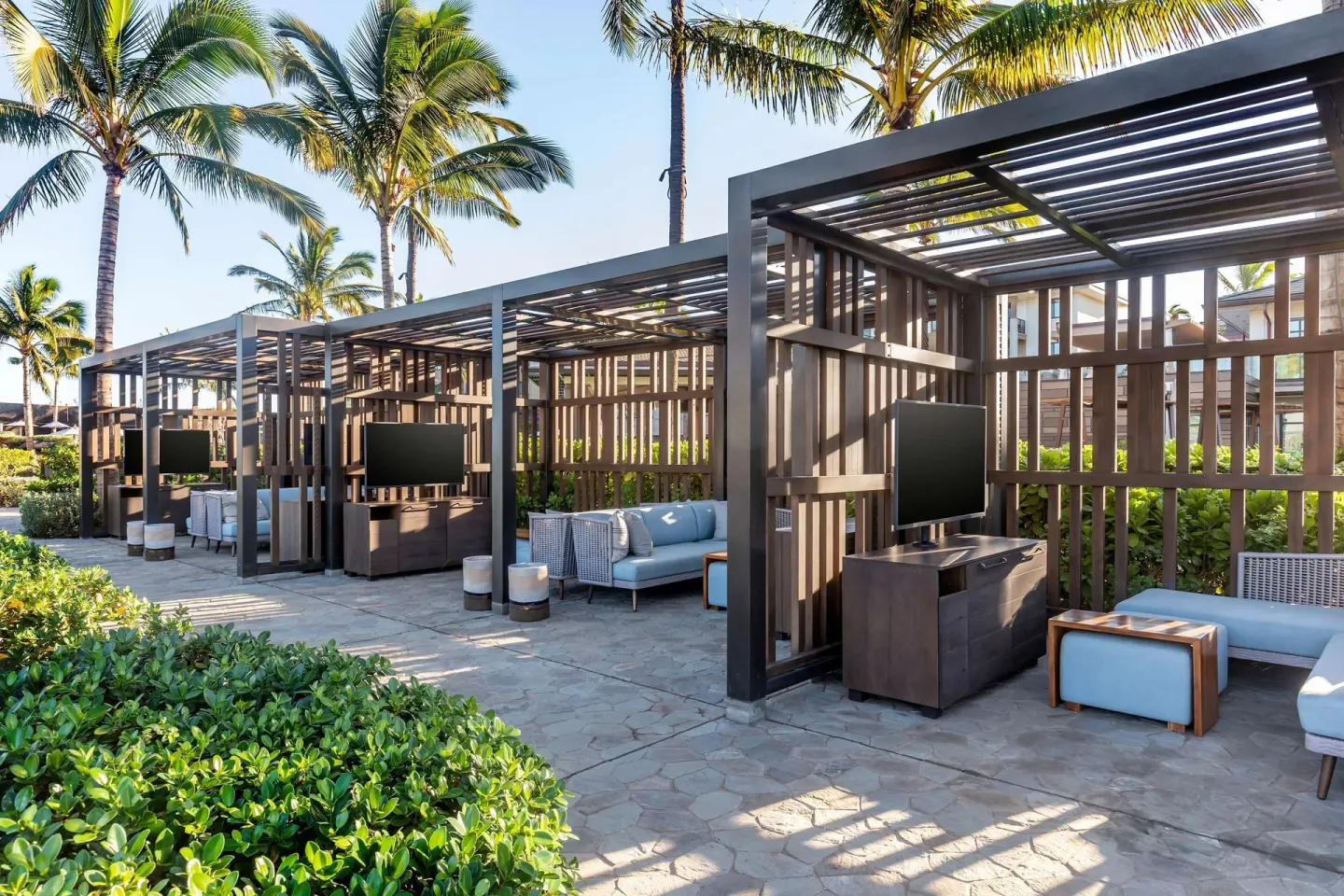 Shaded outdoor cabanas at Hilton Grand Vacations Club Maui Bay Villas with sofas, tables, and televisions.