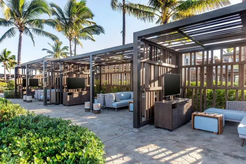 Shaded outdoor cabanas at Hilton Grand Vacations Club Maui Bay Villas with sofas, tables, and televisions.