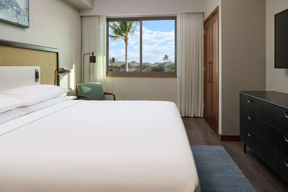 One-bedroom suite with king bed and palm-view window at Hilton Grand Vacations Club Maui Bay Villas.