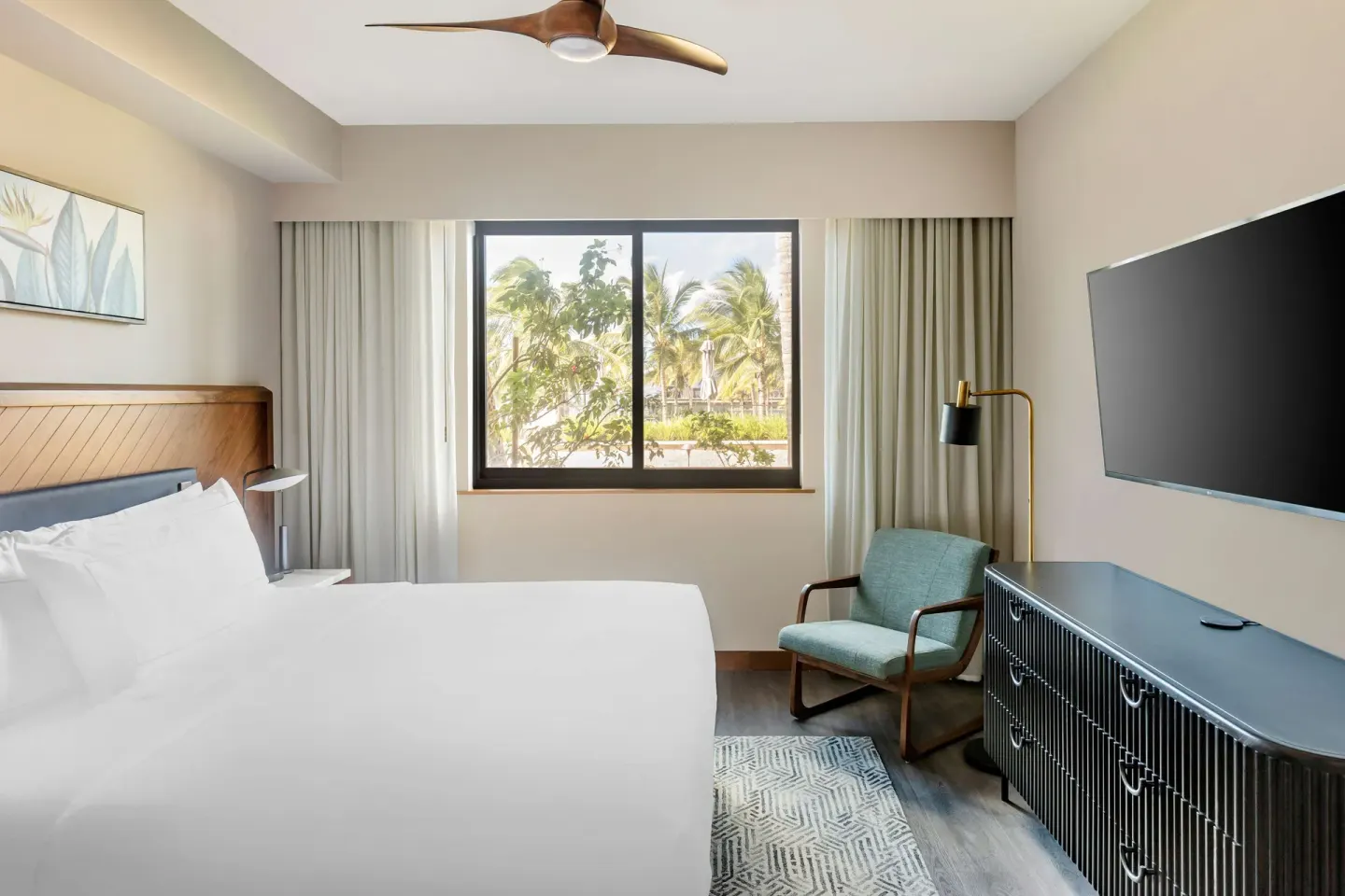 Bedroom with king bed, TV, armchair, and palm view at Hilton Grand Vacations Club Maui Bay Villas.