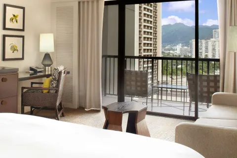 Guest room with balcony views of Waikiki buildings and mountains at Hilton Hawaiian Village Waikiki Beach Resort.