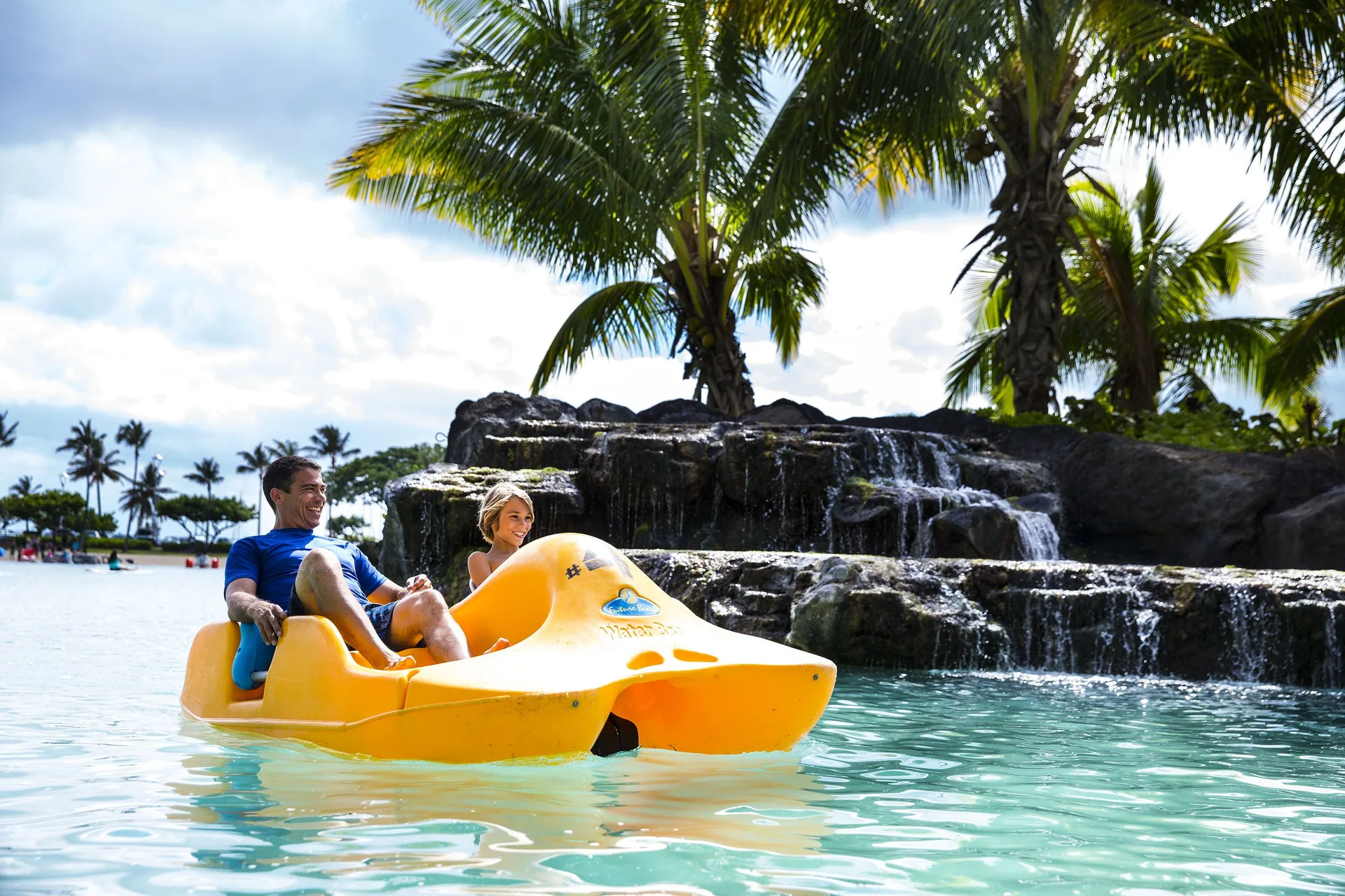 Couple in a pedal boat near a lagoon waterfall at Hilton Hawaiian Village Waikiki Beach Resort.