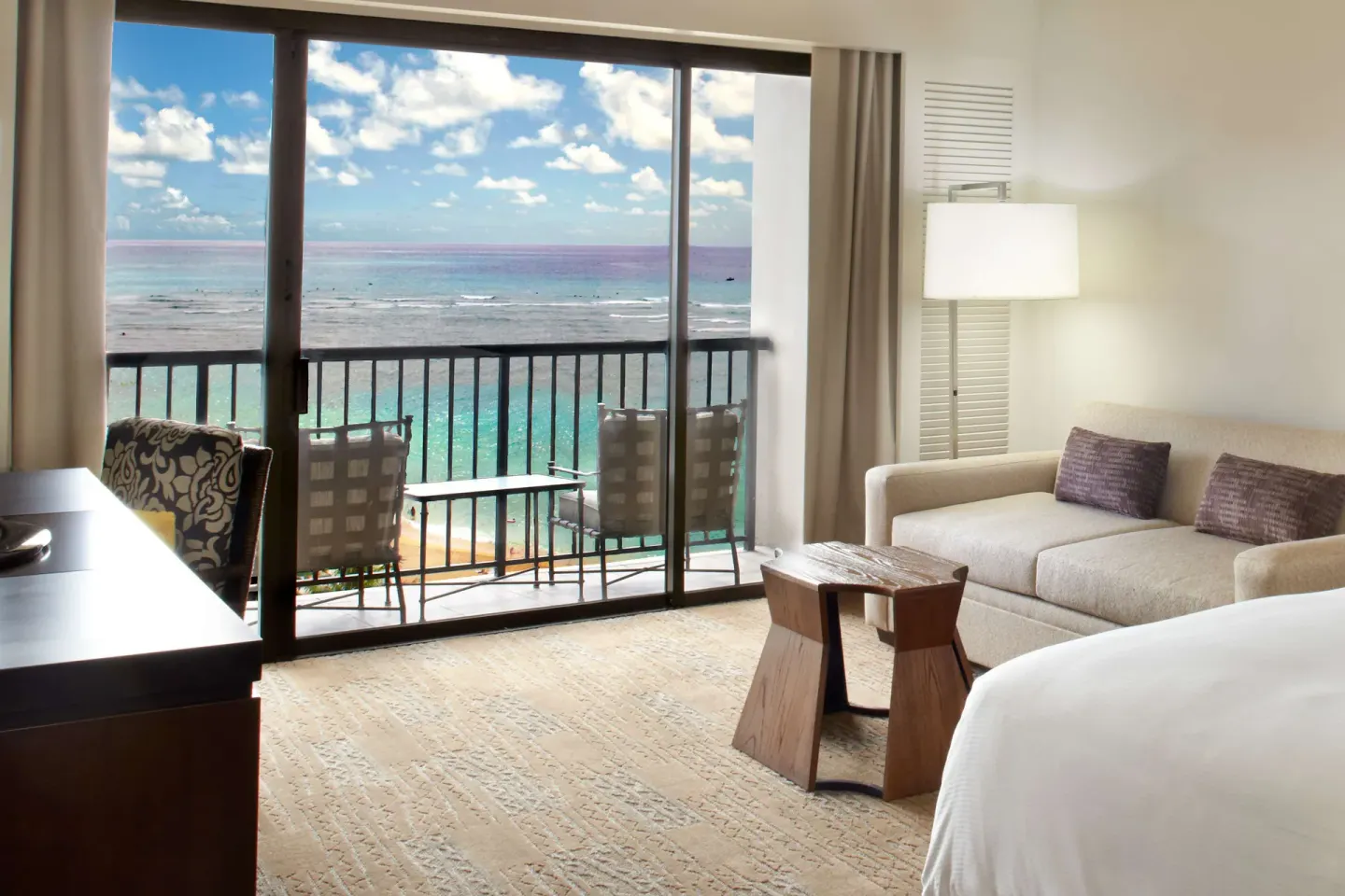 Guest room sofa, bed, and balcony facing the ocean at Hilton Hawaiian Village Waikiki Beach Resort.