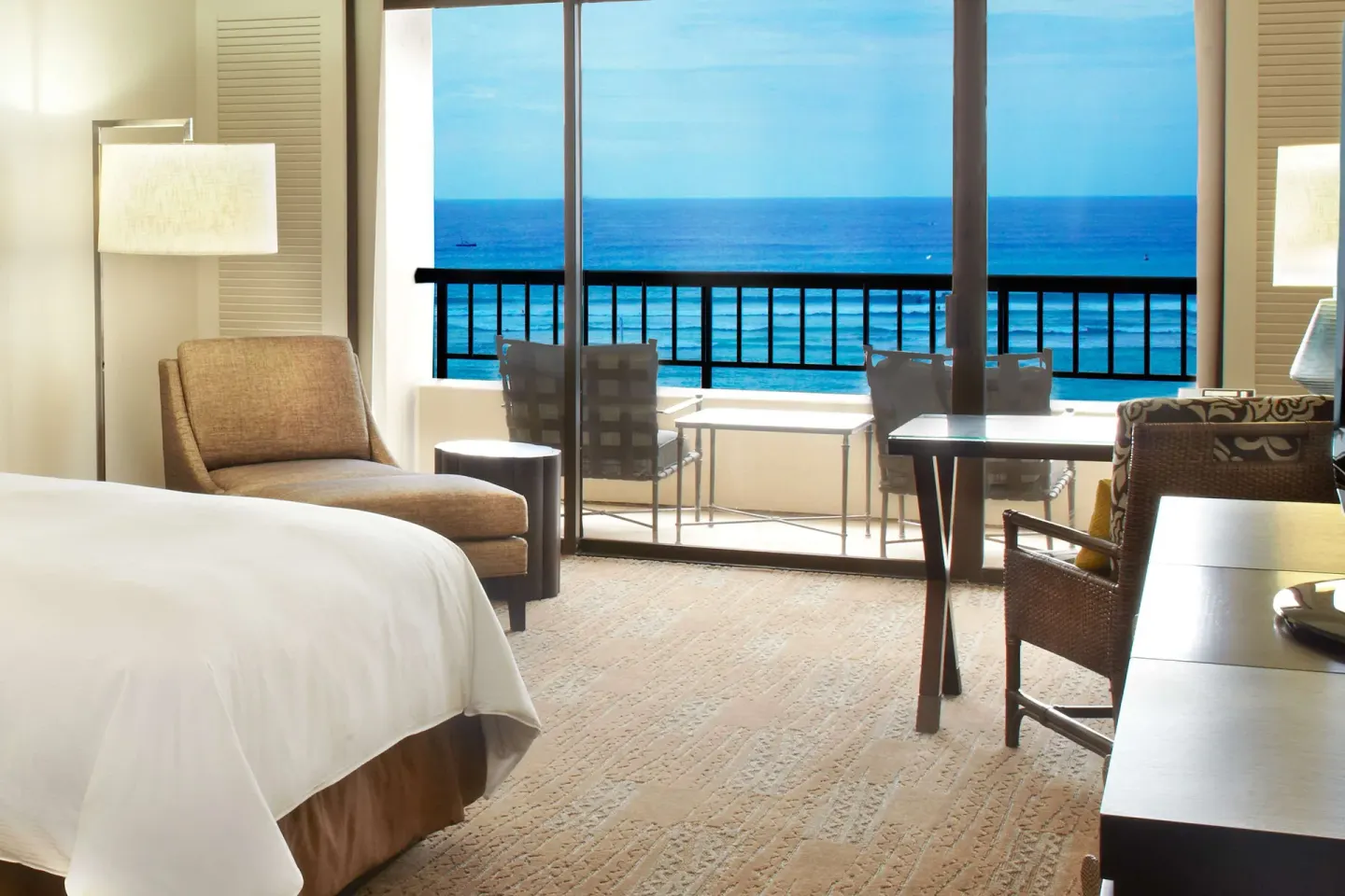 Ocean view guest room with bed, armchair, desk, and balcony at Hilton Hawaiian Village Waikiki Beach Resort.