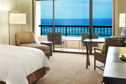 Ocean view guest room with bed, armchair, desk, and balcony at Hilton Hawaiian Village Waikiki Beach Resort.