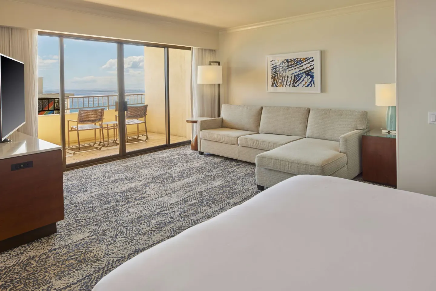 Guest room sitting area with sofa, bed, TV, and ocean balcony at Hilton Hawaiian Village Waikiki Beach Resort.