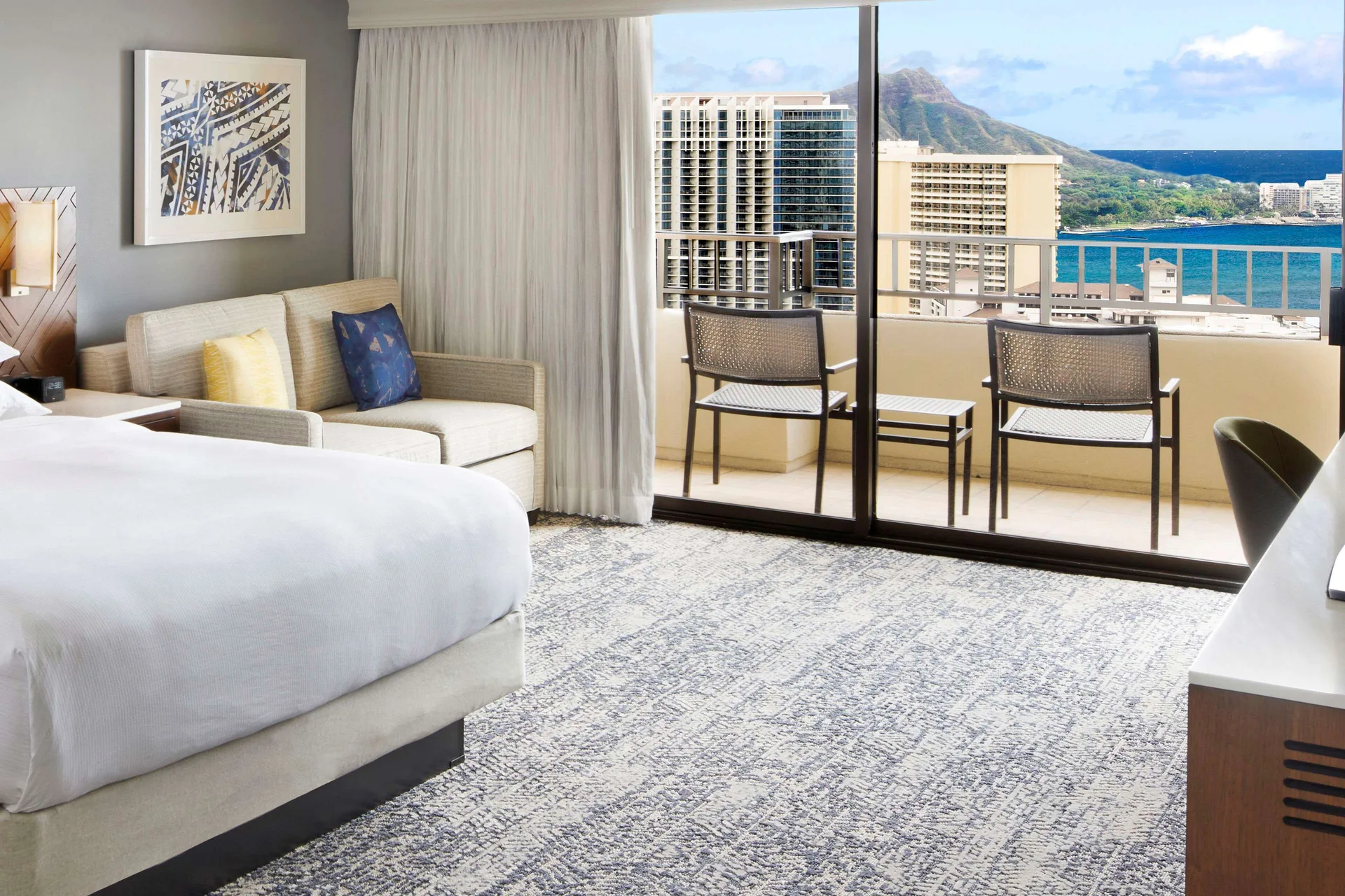 Ocean View Tapa Collection guest room with bed, sofa, balcony, and ocean at Hilton Hawaiian Village Waikiki Beach Resort.