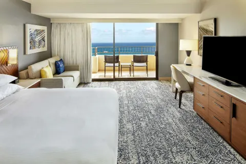 Ocean view guest room with bed, sofa, desk, and balcony at Hilton Hawaiian Village Waikiki Beach Resort.