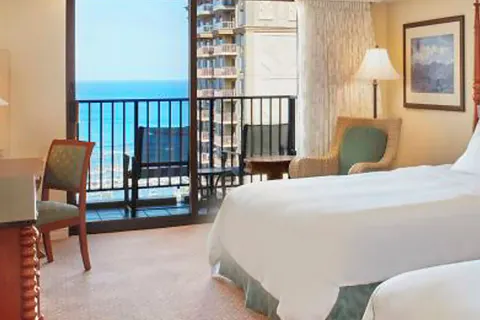 Ocean View room with bed, chair, desk, and balcony at Hilton Hawaiian Village Waikiki Beach Resort.