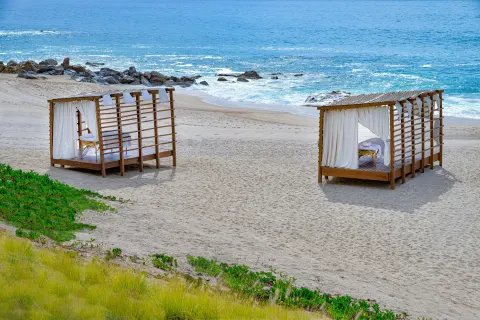 Two curtained beach cabanas set on the sand by the ocean at Hilton Los Cabos.