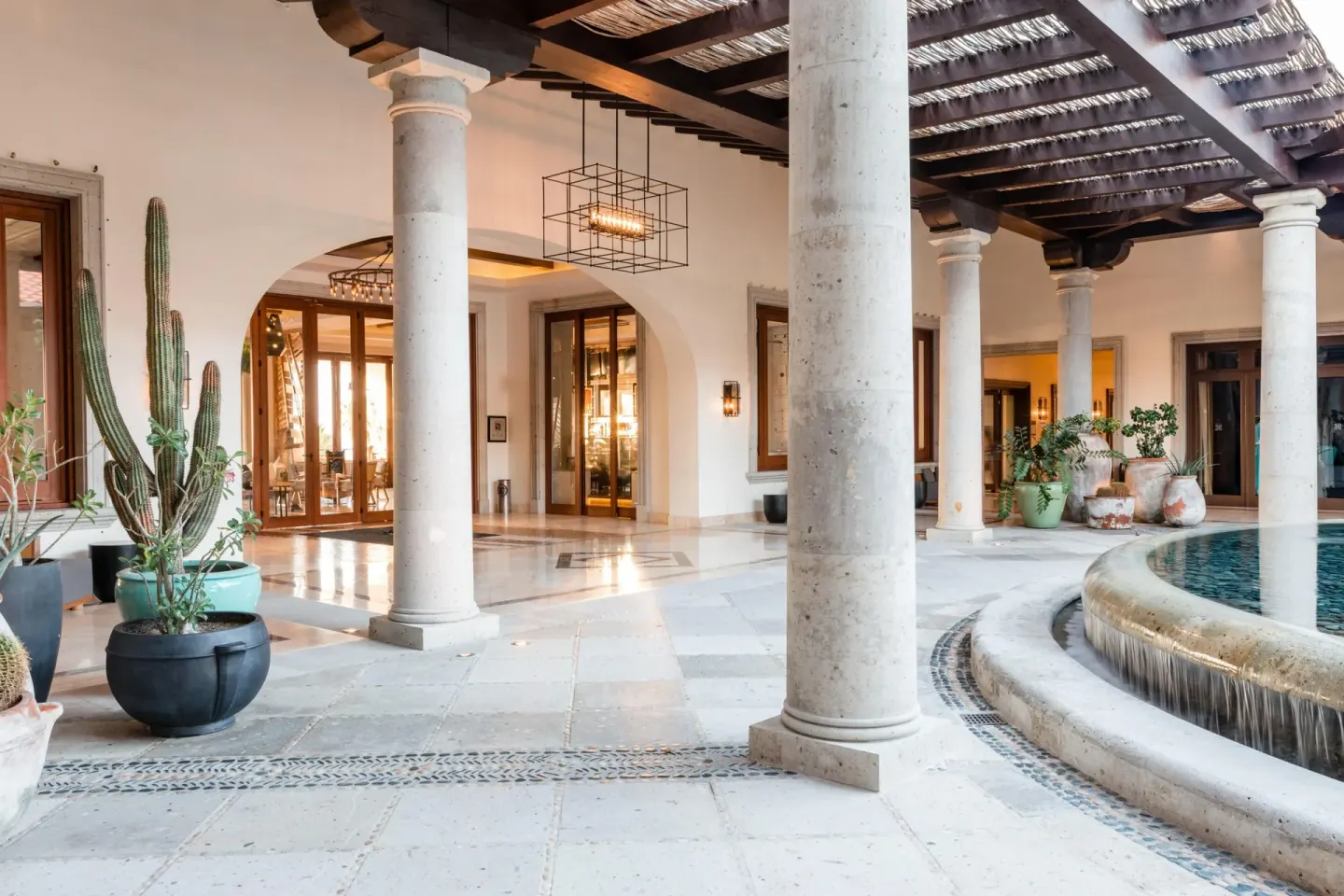 Covered lobby terrace with columns, potted cacti, and a round fountain at Hilton Los Cabos.