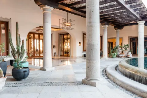 Covered lobby terrace with columns, potted cacti, and a round fountain at Hilton Los Cabos.