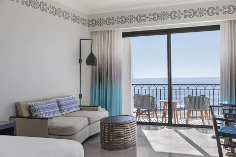 Guest room seating area and balcony chairs facing the ocean at Hilton Los Cabos.