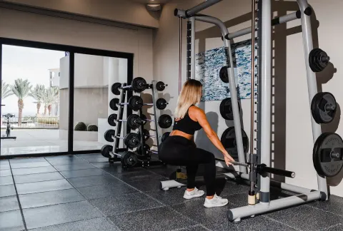 Indoor gym with weights and a guest lifting a barbell at Hilton Los Cabos.