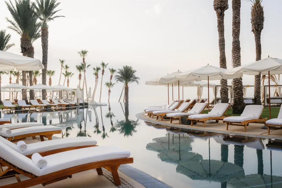 Pool deck with white loungers, umbrellas and palm reflections at Hilton Los Cabos.