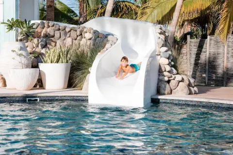 Child sliding down a white pool slide into the water at Hilton Los Cabos.