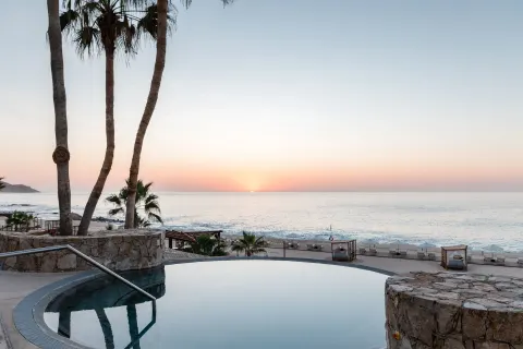 Sunset over the ocean beyond a round pool and palms at Hilton Los Cabos.