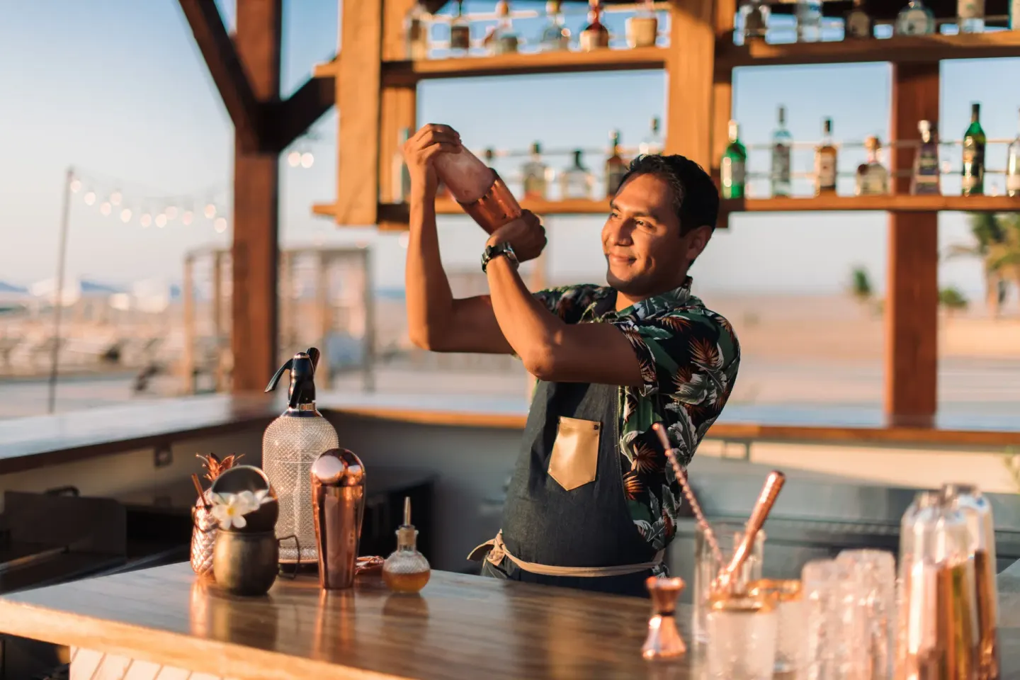 Bartender shaking a cocktail behind an open-air beach bar at Hilton Los Cabos.