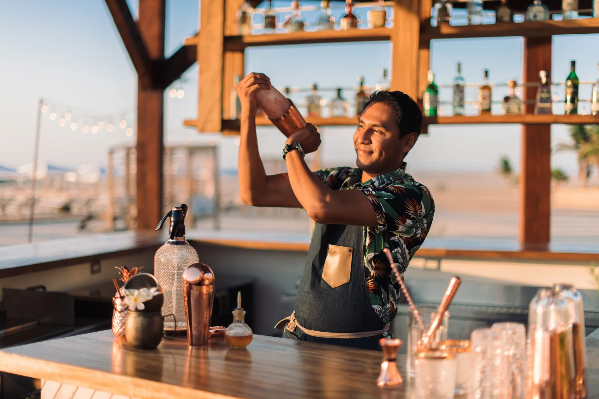 Bartender shaking a cocktail behind an open-air beach bar at Hilton Los Cabos.