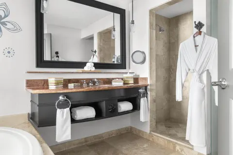 Altamar Junior Suite bathroom vanity with walk-in shower and robe at Hilton Los Cabos.
