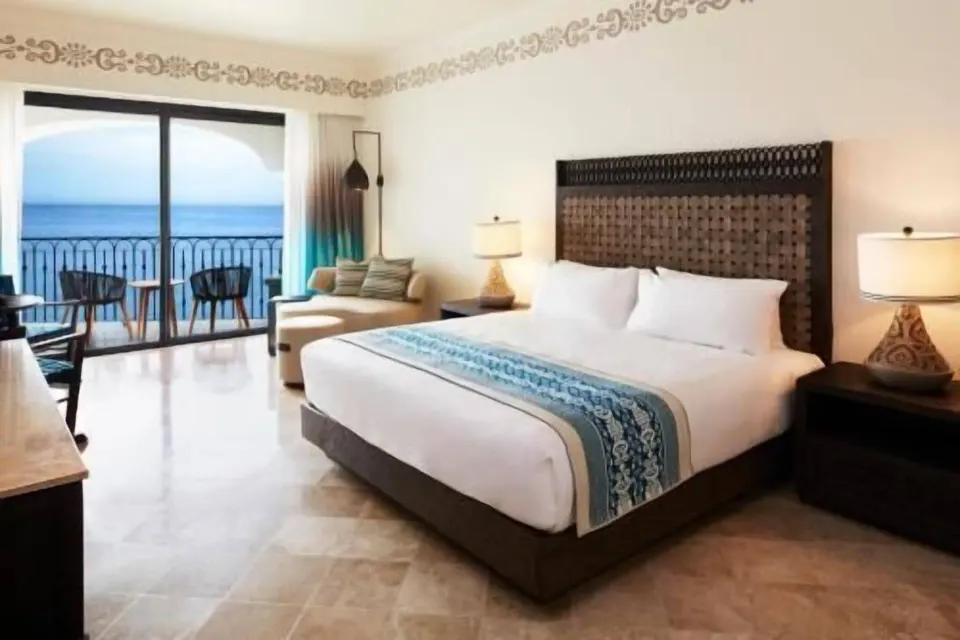 Deluxe Room Coastal Garden View king bed at Hilton Los Cabos facing a balcony and ocean.