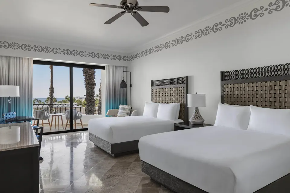 Deluxe Room with two beds, balcony seating, and ocean glimpse at Hilton Los Cabos.