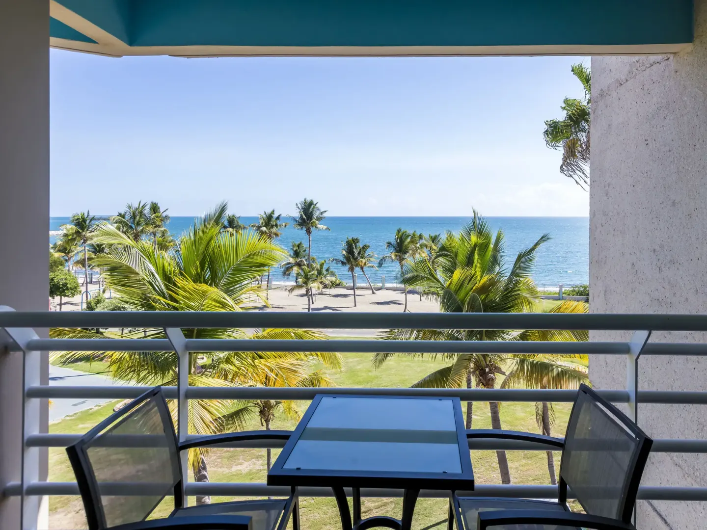 Balcony table and chairs overlooking palms and the ocean at Hilton Ponce Golf & Casino Resort.