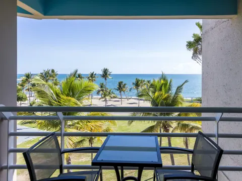 Balcony table and chairs overlooking palms and the ocean at Hilton Ponce Golf & Casino Resort.