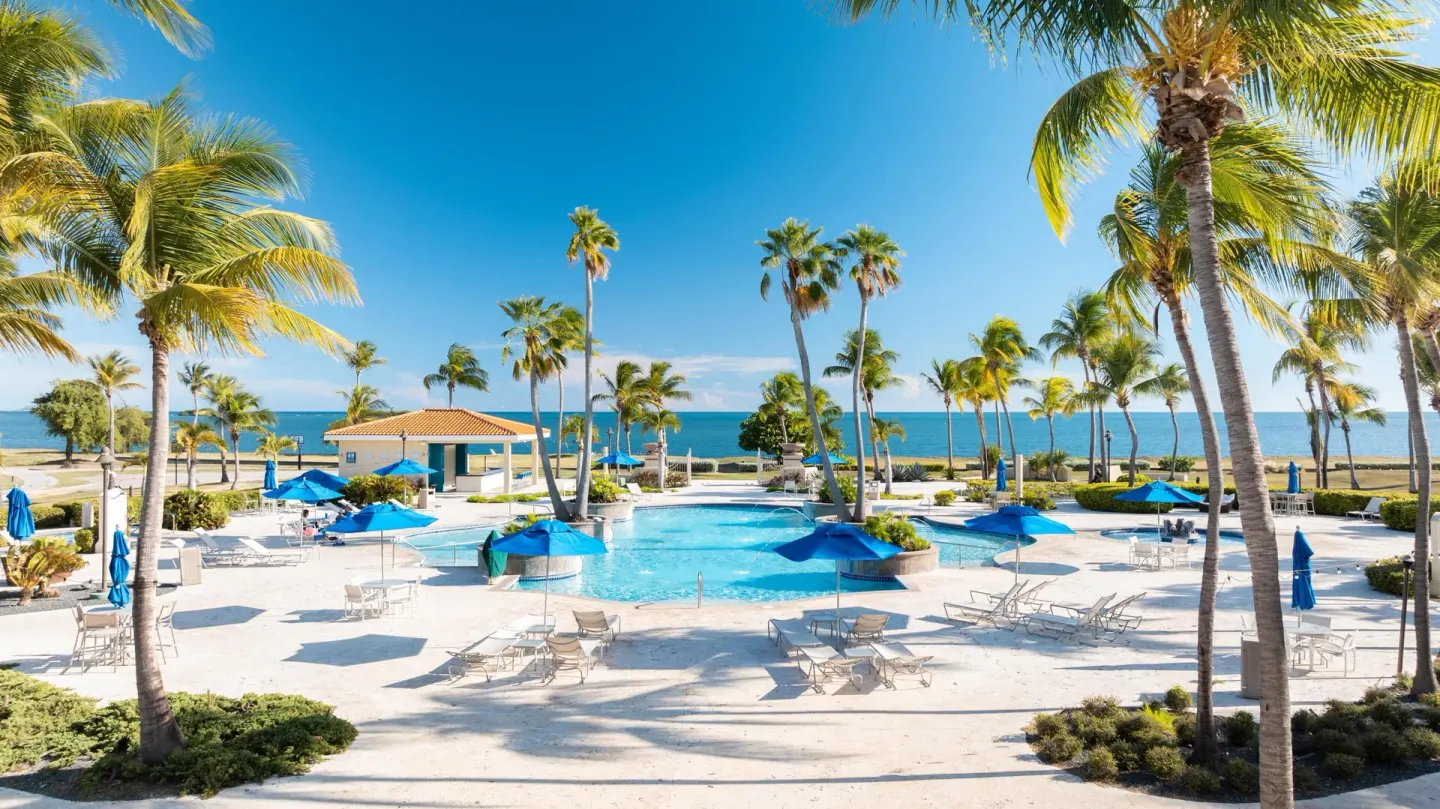 Pool deck with blue umbrellas, palms and ocean beyond at Hilton Ponce Golf & Casino Resort.