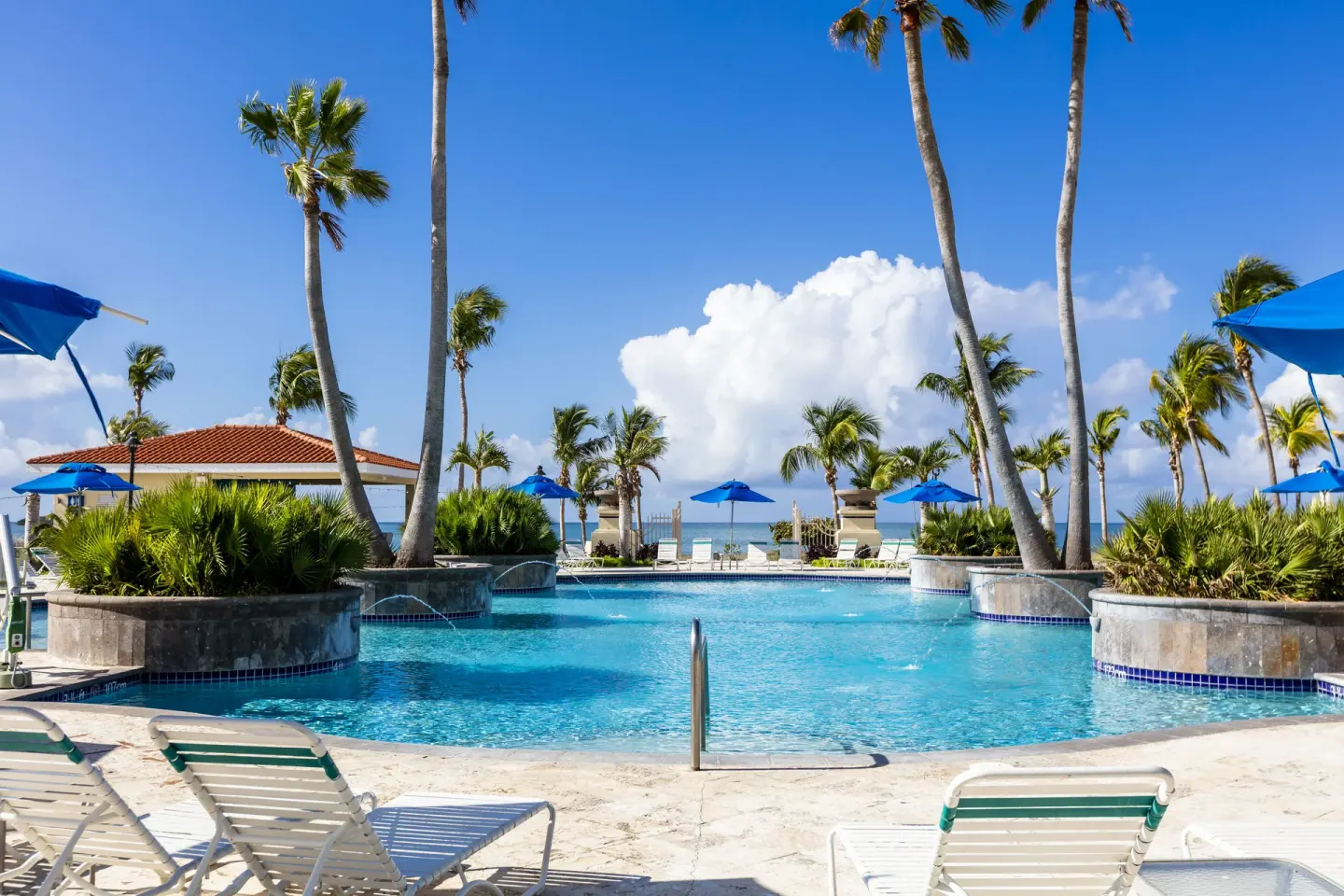 Pool with lounge chairs, palms, and ocean view at Hilton Ponce Golf & Casino Resort.