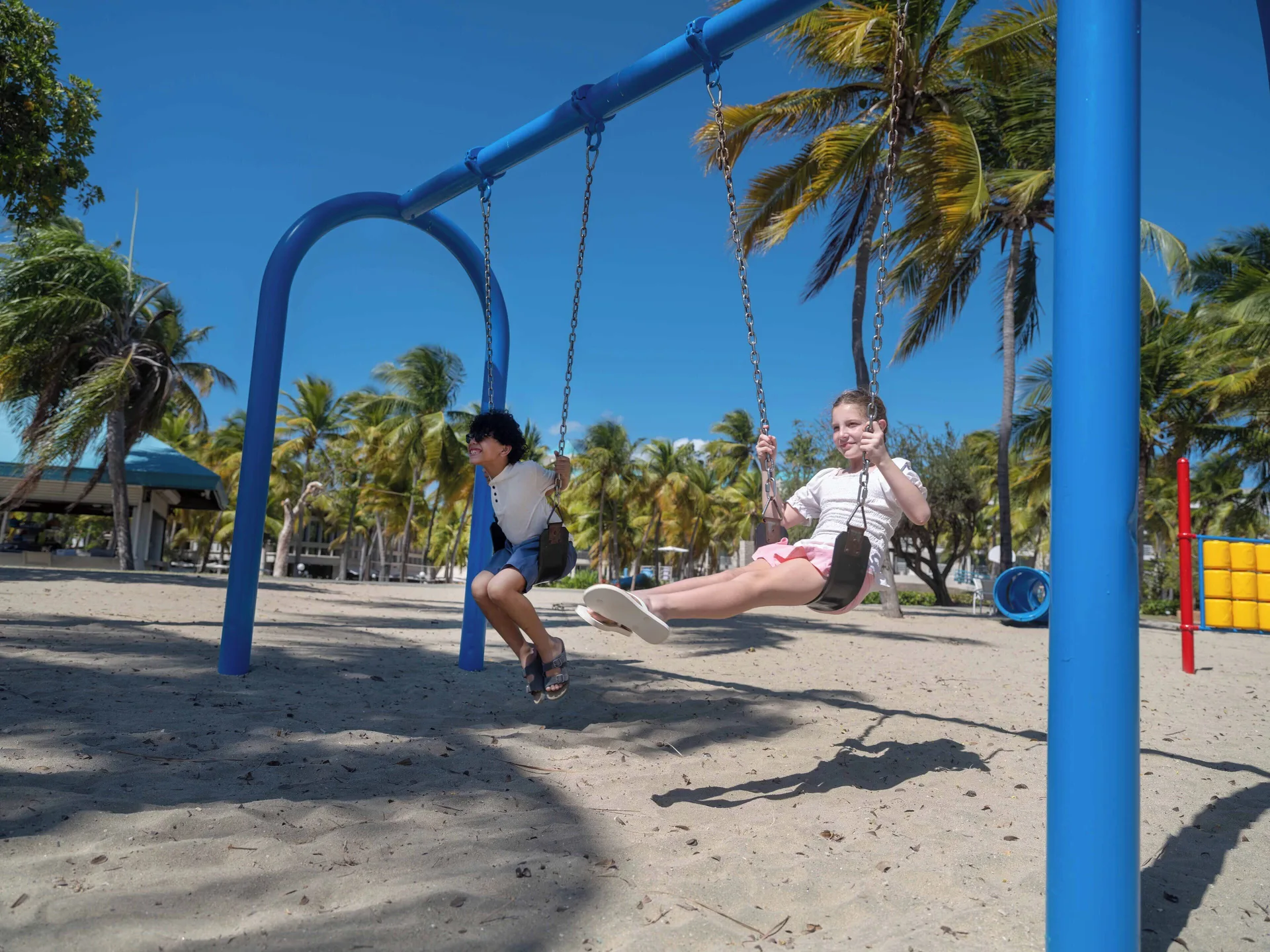 Children swing on a sandy playground under palms at Hilton Ponce Golf & Casino Resort.