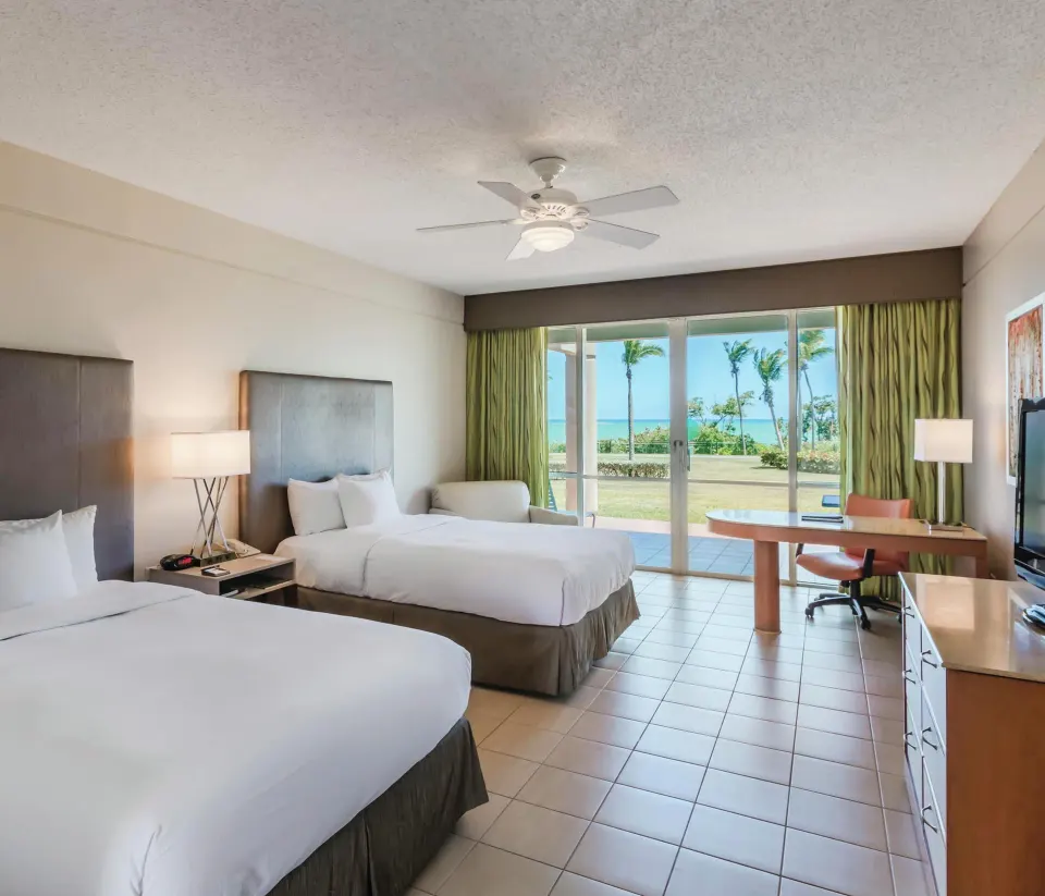 Oceanfront deluxe patio room with two beds and ocean-facing doors at Hilton Ponce Golf & Casino Resort.