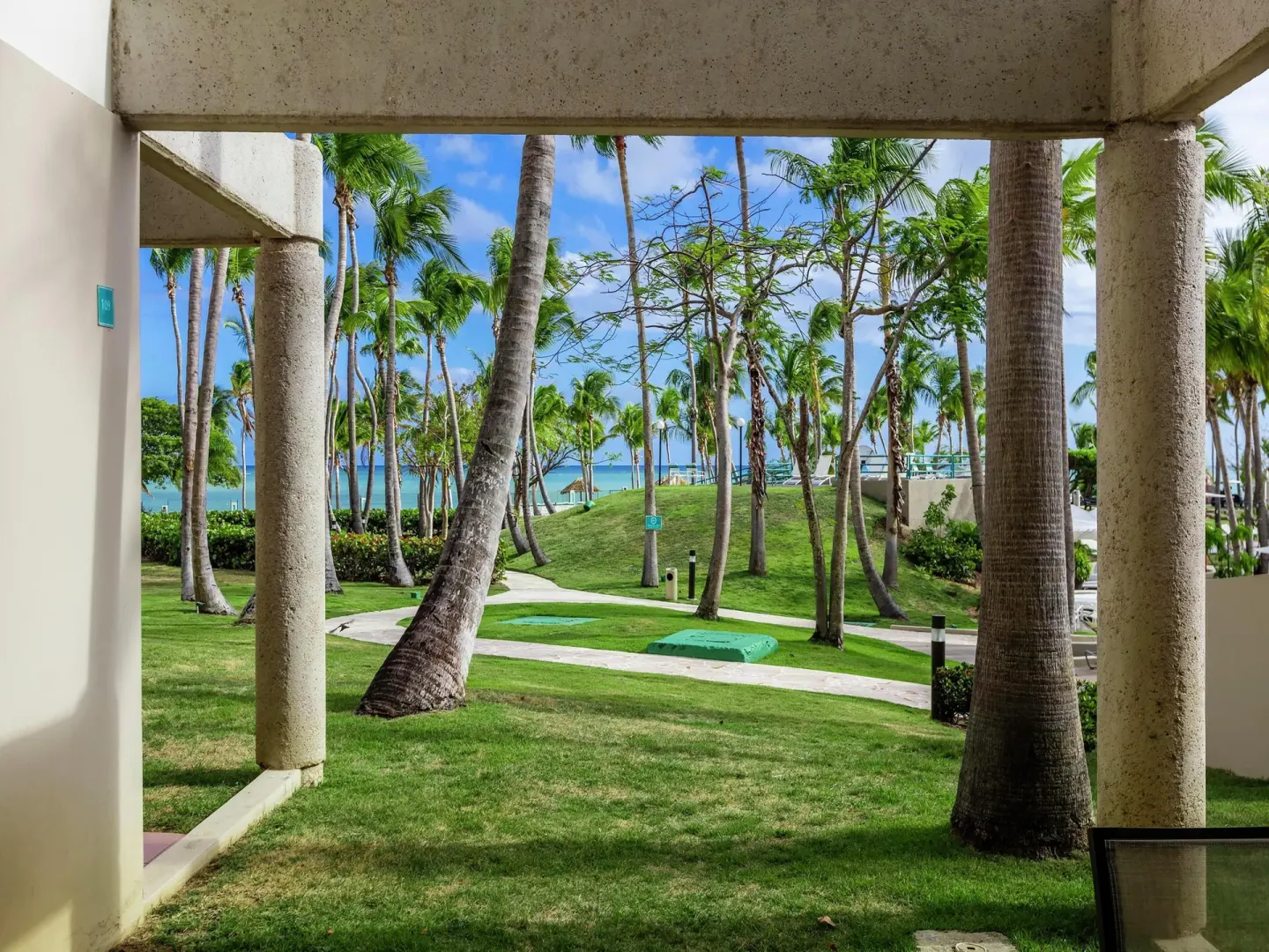 Oceanfront patio view at Hilton Ponce Golf & Casino Resort with palms, lawn, paths, and ocean beyond.