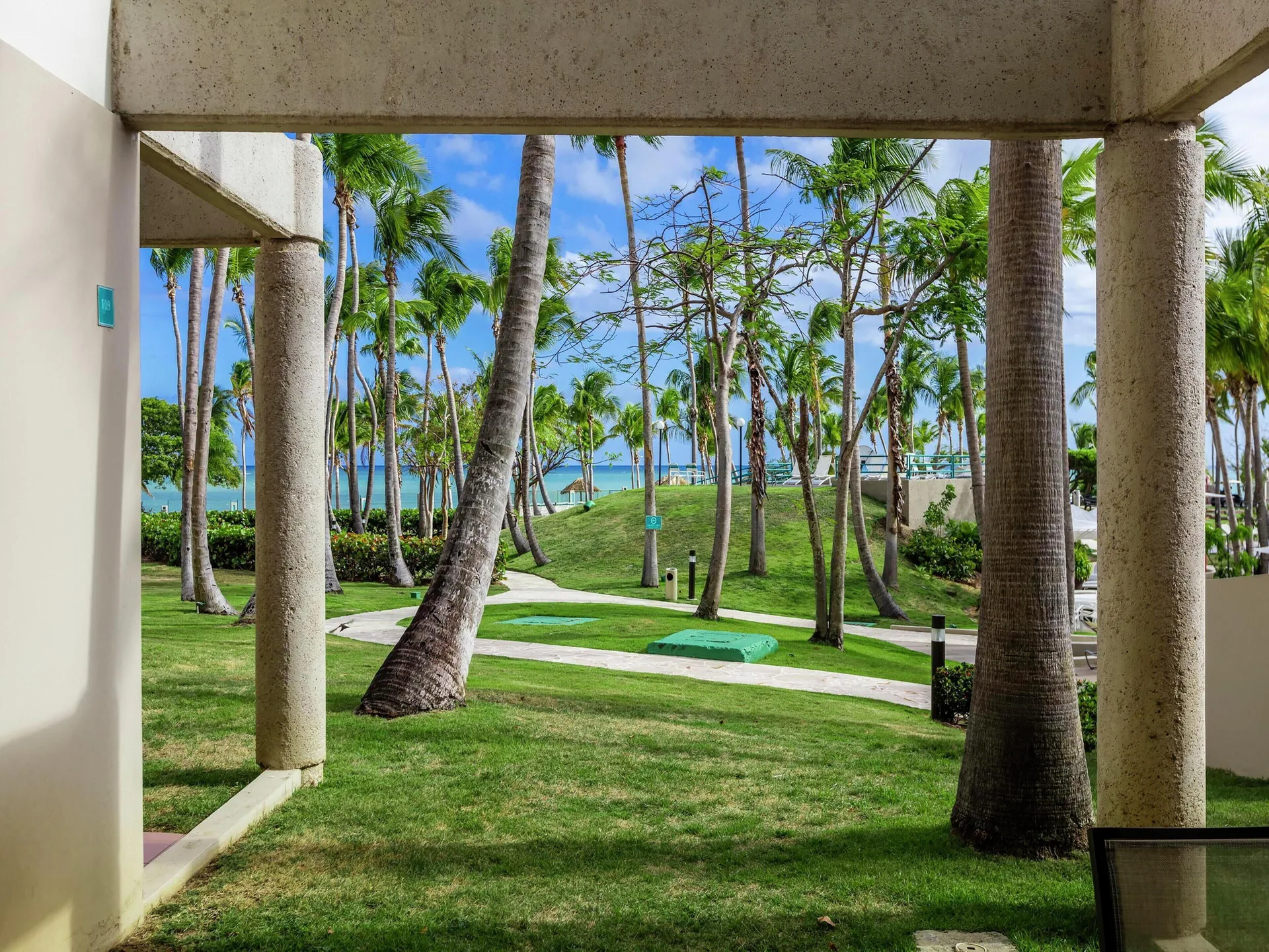 Oceanfront patio view at Hilton Ponce Golf & Casino Resort with palms, lawn, paths, and ocean beyond.