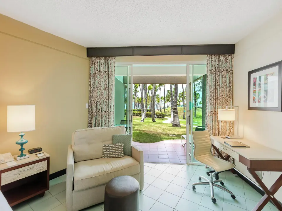 Oceanfront patio room sitting area at Hilton Ponce Golf & Casino Resort with desk and open patio doors.