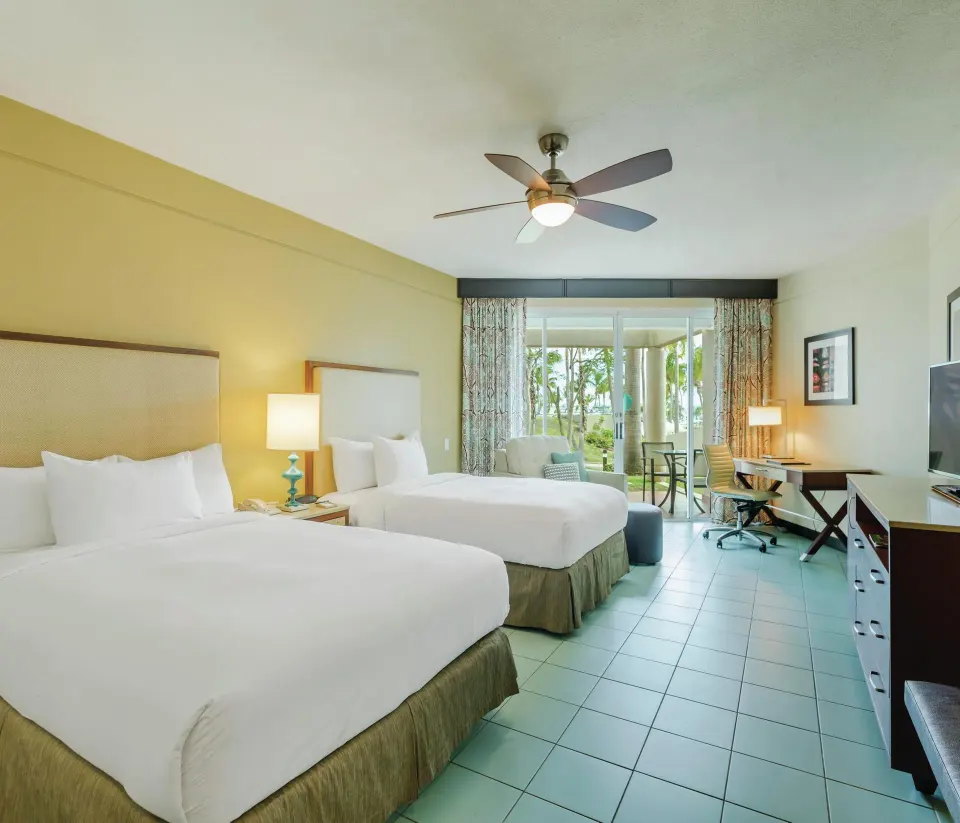 Two-bed oceanfront patio room at Hilton Ponce Golf & Casino Resort with desk, TV, and patio beyond.
