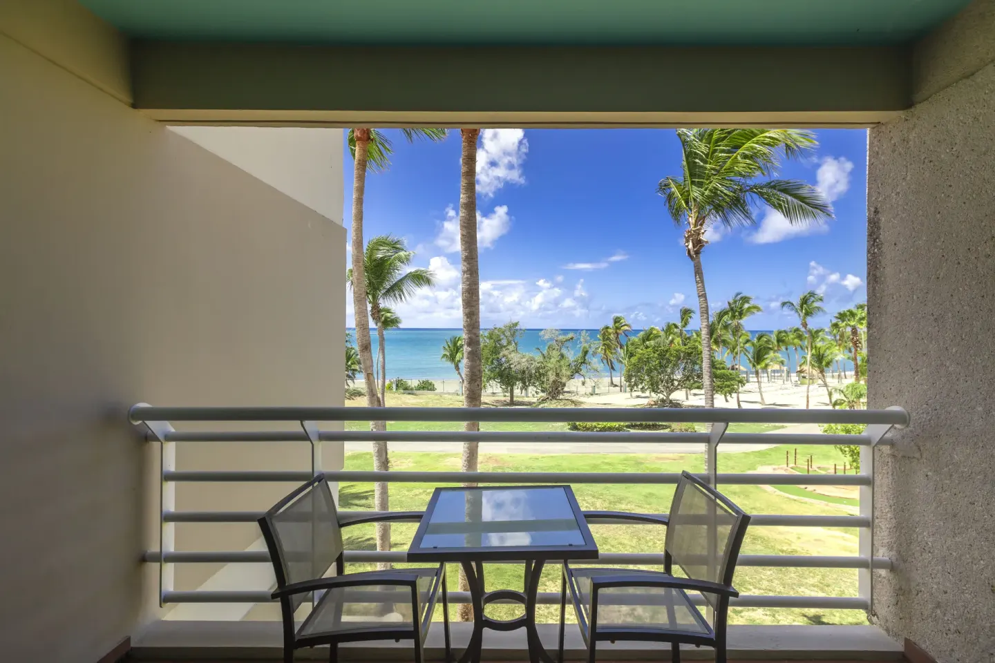 Oceanview mobility room balcony at Hilton Ponce Golf & Casino Resort with chairs, table, palms, and sea.