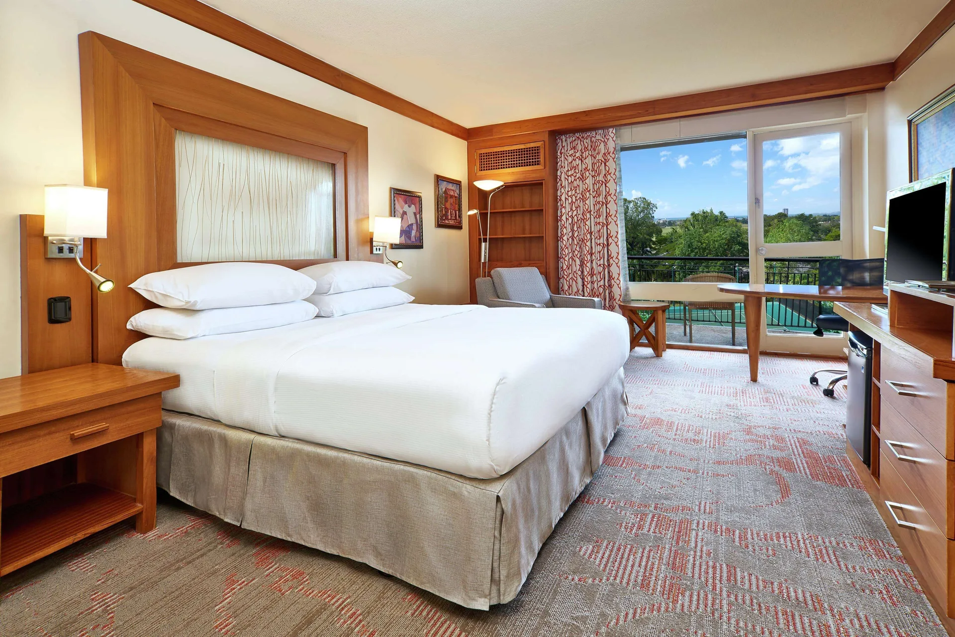 Guest room with king bed, desk, and balcony view at Hilton Trinidad & Conference Centre.