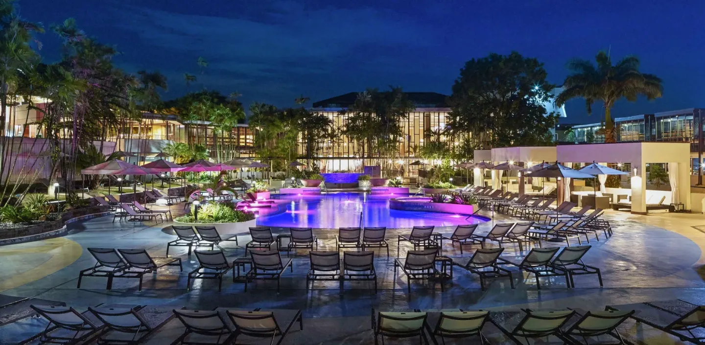 Nighttime pool deck with lounge chairs at Hilton Trinidad & Conference Centre.
