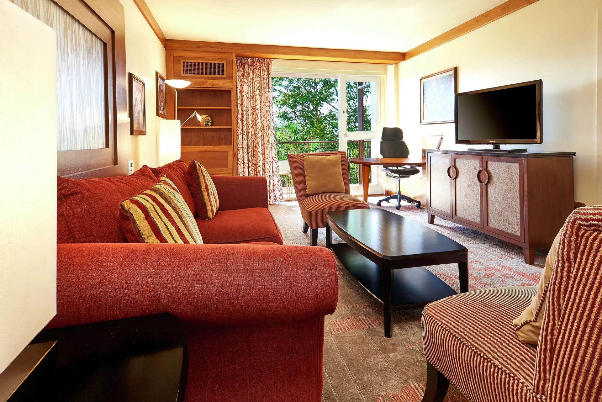 Junior Suite 1 Bedroom 2 Balconies living room with red sofa, desk, and TV at Hilton Trinidad and Conference Centre.