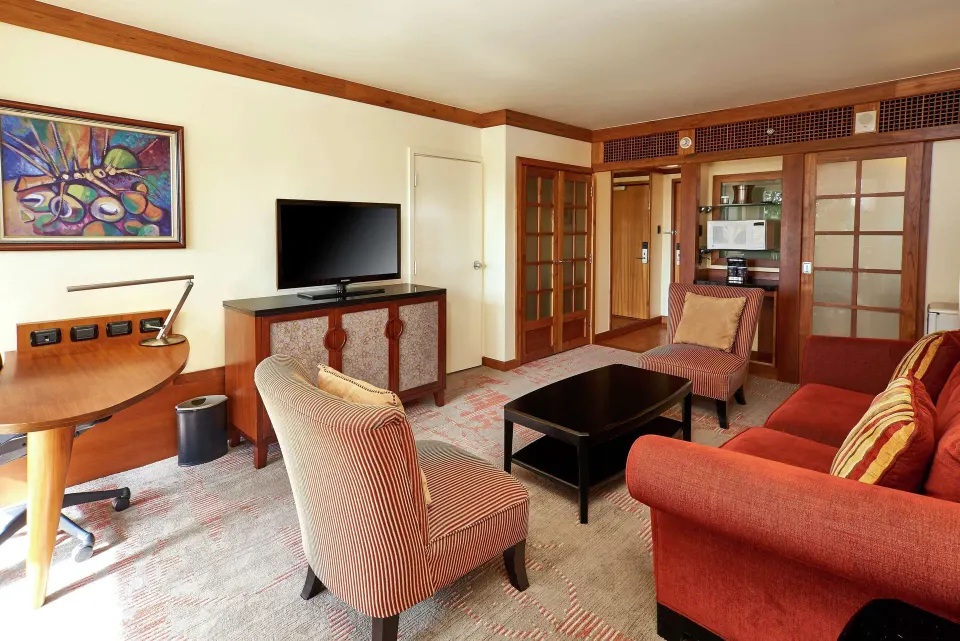 Suite living room with sofa, chairs, desk, and TV at Hilton Trinidad & Conference Centre.