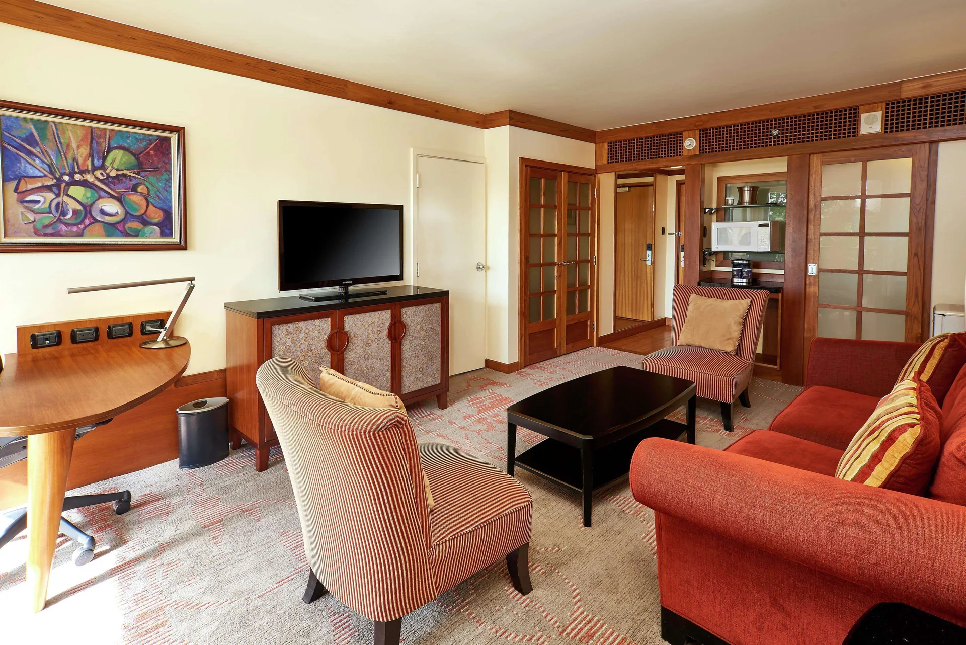 Suite living room with sofa, chairs, desk, and TV at Hilton Trinidad & Conference Centre.