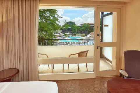 Deluxe Pool View room at Hilton Trinidad & Conference Centre looking out to a balcony and pool area.