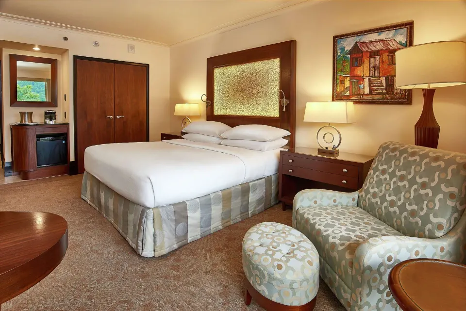 King-bed Deluxe Pool View room at Hilton Trinidad & Conference Centre with lounge chair and ottoman.