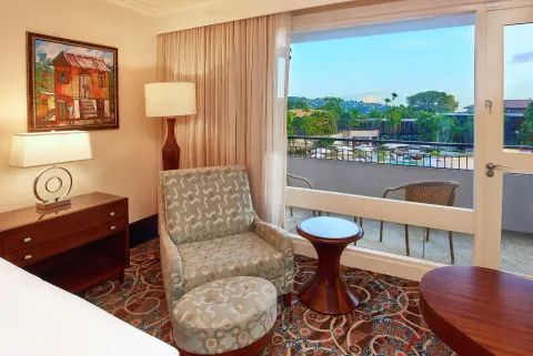 Deluxe Pool View room at Hilton Trinidad & Conference Centre with chair by a balcony overlooking the pool.