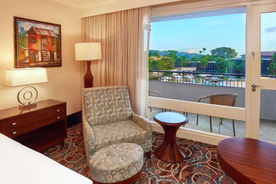 Deluxe Pool View room at Hilton Trinidad & Conference Centre with chair by a balcony overlooking the pool.