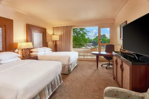 Two-bed Deluxe Pool View room at Hilton Trinidad & Conference Centre with desk, TV, and balcony view.