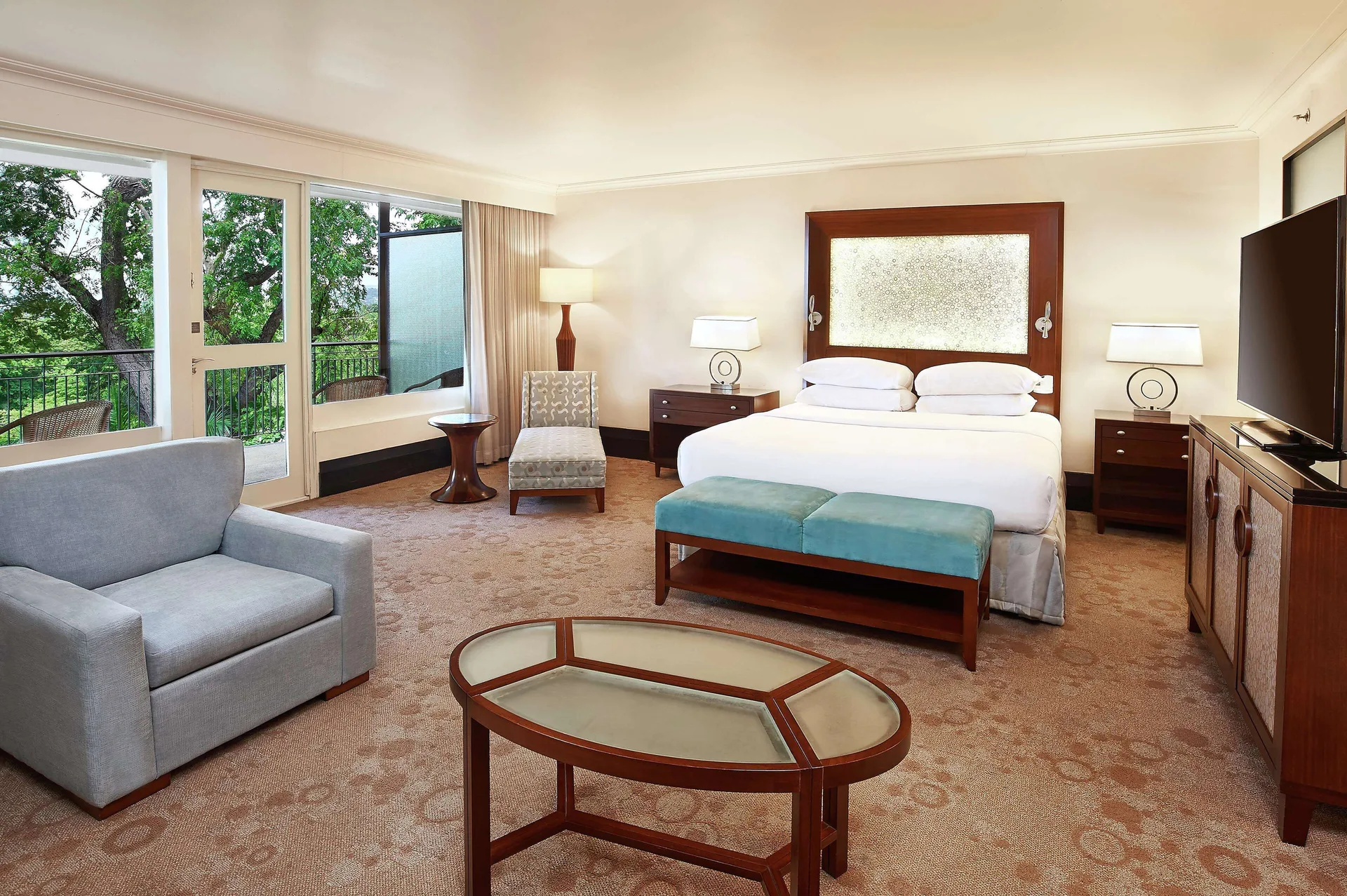 Deluxe Studio Suite king bed with seating area and balcony doors at Hilton Trinidad & Conference Centre.